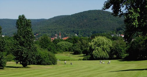 [billede: golfspillere på banen, en by og bjerge i baggrund]